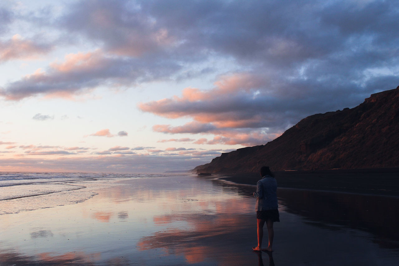 sky, cloud - sky, water, standing, sunset, real people, beauty in nature, scenics - nature, sea, one person, beach, lifestyles, rear view, nature, leisure activity, land, full length, idyllic, outdoors, horizon over water