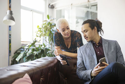 Woman showing mobile phone to colleague in office