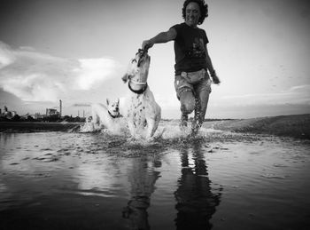 Woman with dogs running on shore at beach against sky during sunset