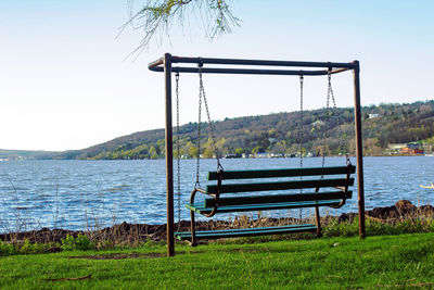 Empty bench by lake against sky