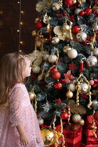 Happy child smiling blond girl in beautiful dress decorating christmas tree