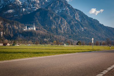 Road amidst field and mountains against sky