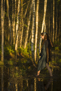 Side view of woman walking in lake against trees at forest