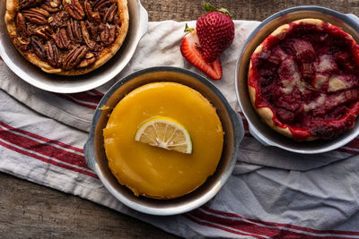 Above artisan baked lemon custard tart, pecan tart, and strawberry tart on retro style kitchen towel