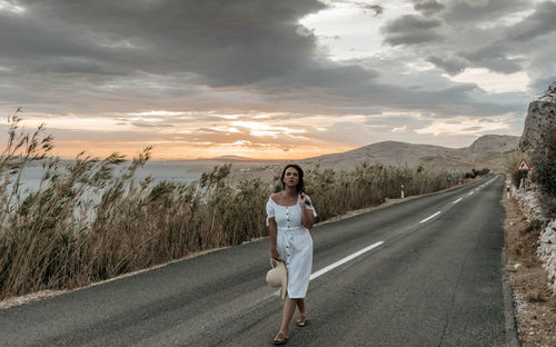 Portrait of woman standing on road against sky during sunset