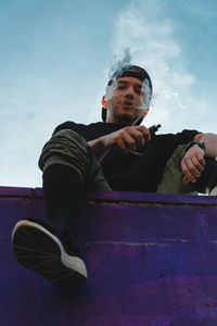 Low angle view of young man sitting on seat against sky