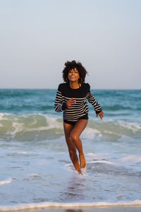 Woman with afro hair having fun at the beach running from the waves