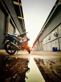 Motorcycle parked on street amidst buildings against sky during sunset