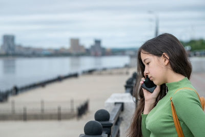 Young woman looking away while standing against sea