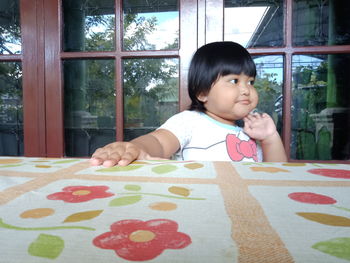 Portrait of cute girl looking through window at home