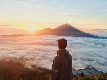 Rear view of man standing on mountain against sky