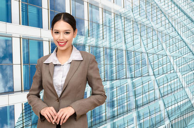 Portrait of smiling young businesswoman standing against buildings