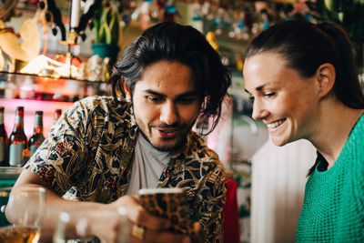 Smiling young man sharing smart phone with woman sitting in restaurant during brunch party