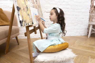 Cute girl drawing rainbow on white sheet on a drawing easel. little painting artist.