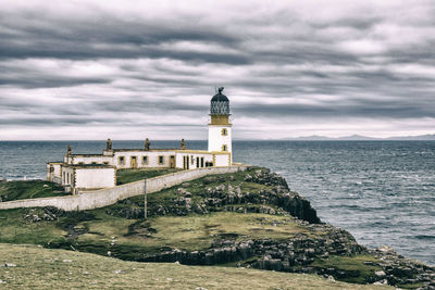 Lighthouse by sea against buildings