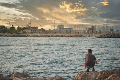 Rear view of man standing by sea against sky during sunset