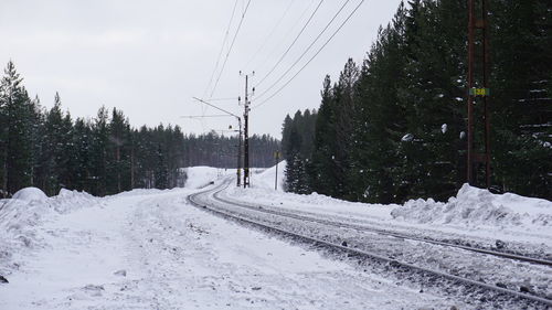 Railroad tracks by snow covered trees against sky