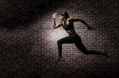 Full length of woman jumping against brick wall