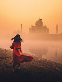 Woman with arms outstretched against sky during sunset