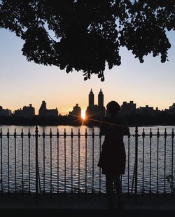 Rear view of silhouette people standing by railing against sunset