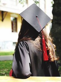 Rear view of woman in graduation gown standing in park