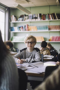 Boy wearing eyeglasses sitting at desk in classroom