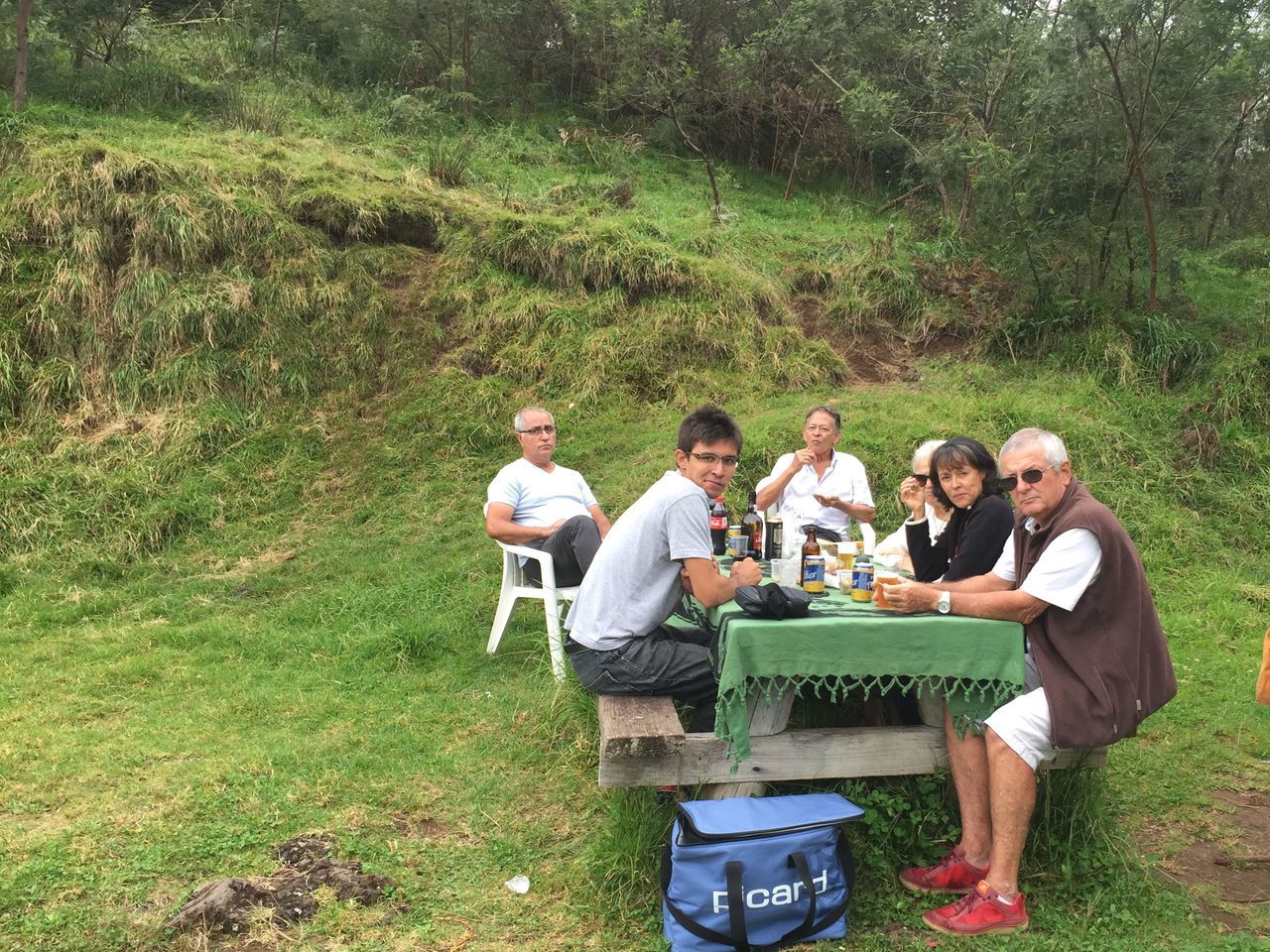 group of people, food and drink, men, smiling, full length, plant, nature, happiness, food, adult, togetherness, women, group, sitting, males, tree, friendship, young men, grass, social gathering, mature adult, picnic, outdoors, meal