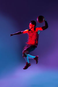 Creative studio shot of basketball player in studio using colored gels and projector lights and jumping with a ball