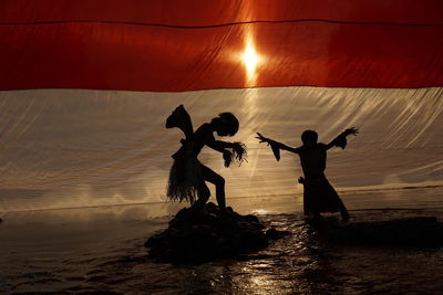 Silhouette people at beach against sky during sunset