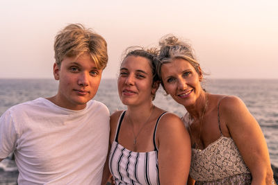 Beautiful mother with her two twenty year old sons take a break by the sea at sunset. summer concept