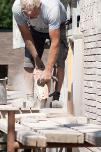 A grayhaired man saw bricks with a concrete saw of the right size for subsequent