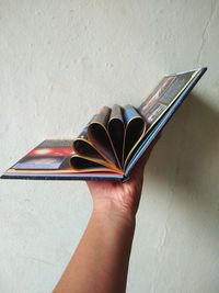 Close-up of hand holding book against wall