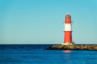 Lighthouse by sea against clear sky