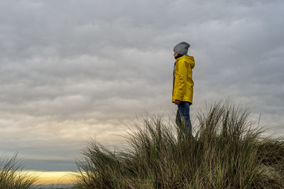 Woman wearing a yellow coat standing on top of a dune, book cover concept.