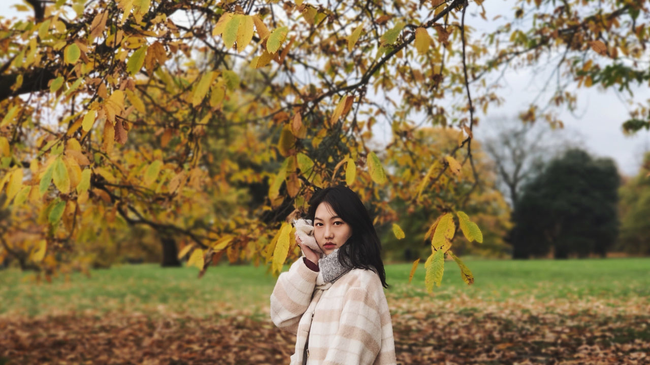 PORTRAIT OF YOUNG WOMAN STANDING BY TREE IN AUTUMN