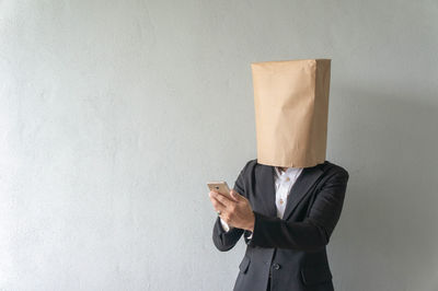 Midsection of man holding mobile phone while standing against wall