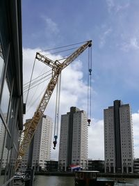 Low angle view of crane and buildings against sky