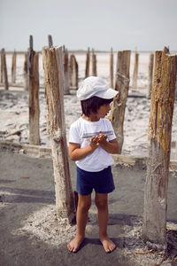 Child boy in a cap t shirt and shorts holds a phone in his hands and stands on a pink lake among 