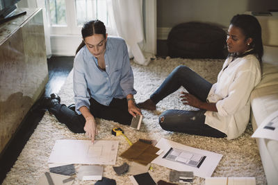 High angle view of female designers discussing about fabric swatch while sitting on carpet at home office