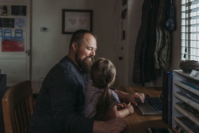 Father with young preschool aged daughter sitting while he works from