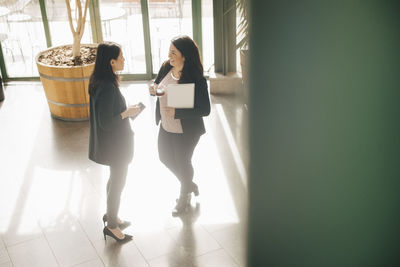 Full length of businesswomen having coffee while discussing in brightly lit workplace