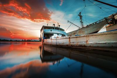 Sailboats moored at harbor against sky during sunset