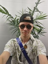 Portrait of young man wearing sunglasses while standing against plant