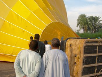 Rear view of people by hot air balloon against sky