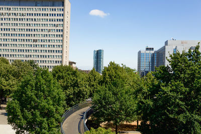 Trees and modern buildings in city against sky