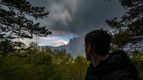 Man looking at rainbow by mountain against cloudy sky