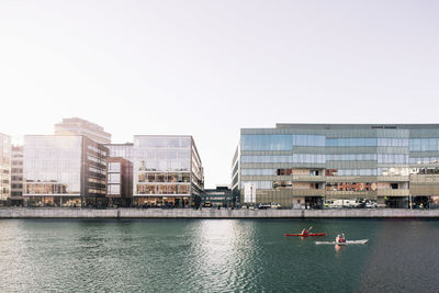 Kayaking over river in city against clear sky