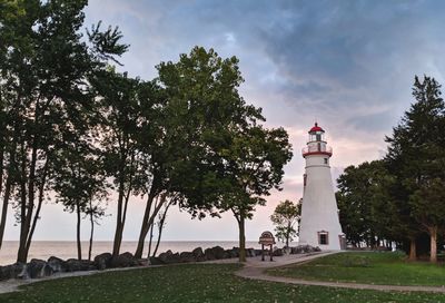 Lighthouse amidst trees and buildings against sky
