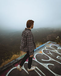 Rear view of man standing on mountain against sky