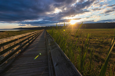 Boardwalk on field against sky during sunset